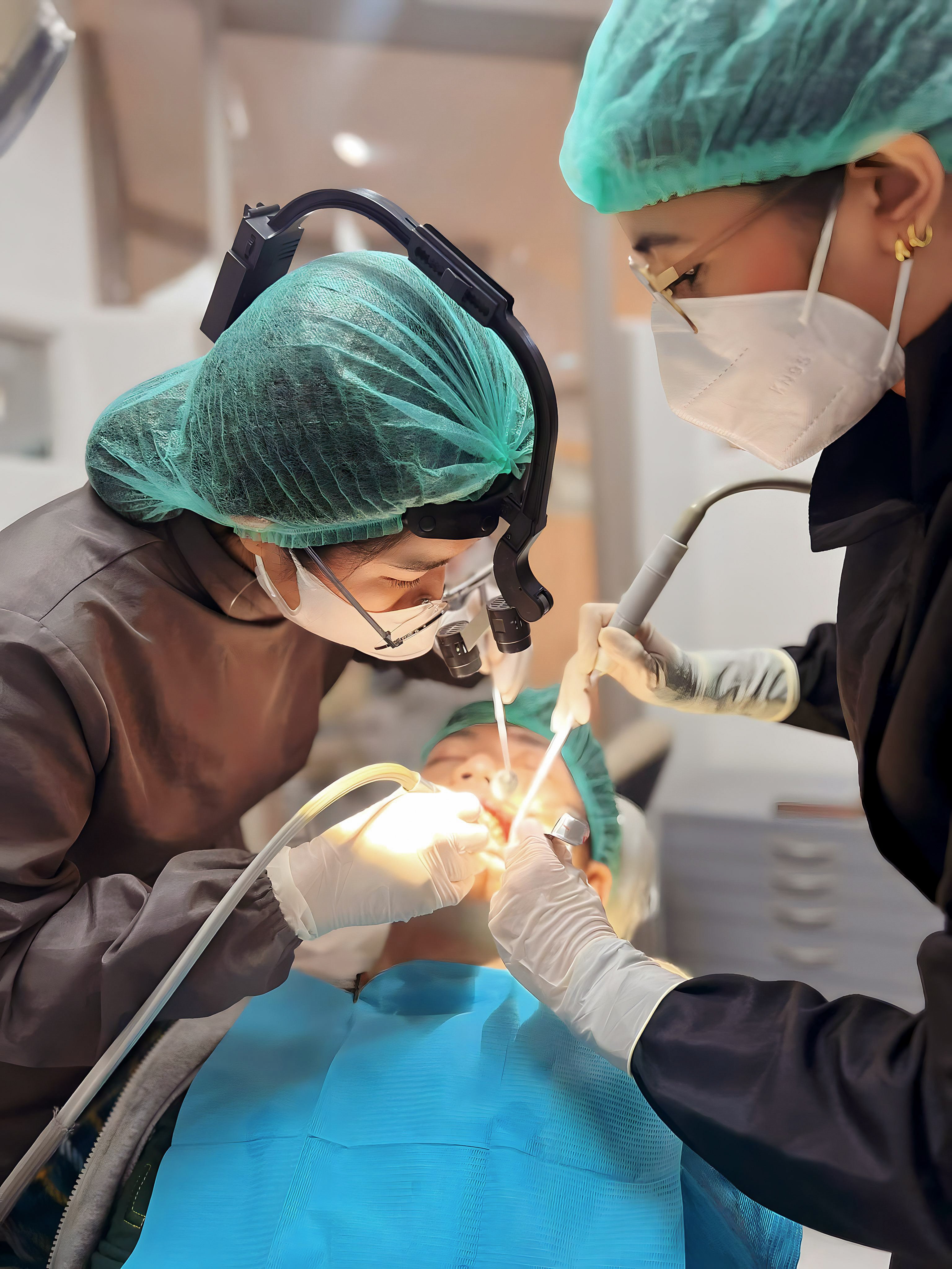 Two dental professionals performing surgery on a patient in a clinical setting.